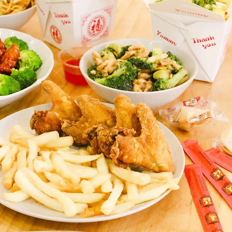 Fried chicken wings, fries, and Chinese dishes on a table at Main Garden, a Chinese Fusion Restaurant in Passaic